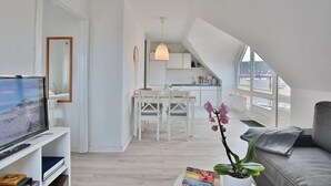 A modern loft apartment with a dining area, kitchen, and a living room with a TV and a couch.