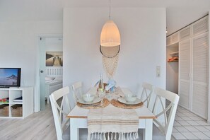 A dining area with a white table set for four, a hanging light fixture, and a television in the background. - Witthus Neue Bergstraße Apartment 14 - Witthus I (Scharbeutz)