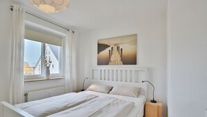 A bedroom with a bed, two bedside tables, a window with curtains, a radiator, and a painting on the wall.