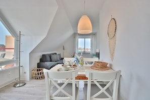 Spiseområde med et hvidt bord og stole, en hængende lampe og udsigt til bybilledet gennem et stort vindue.