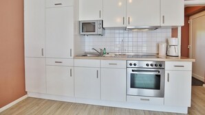 A compact kitchen with white cabinets, a microwave, a stove, and a coffee maker. - Beach villa apartment 6 - Beach villa (Scharbeutz)