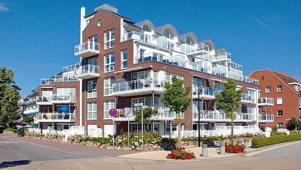 A multi-story residential building with balconies, a clear sky, and a well-maintained garden area. - Beach villa apartment 6 - Beach villa (Scharbeutz)