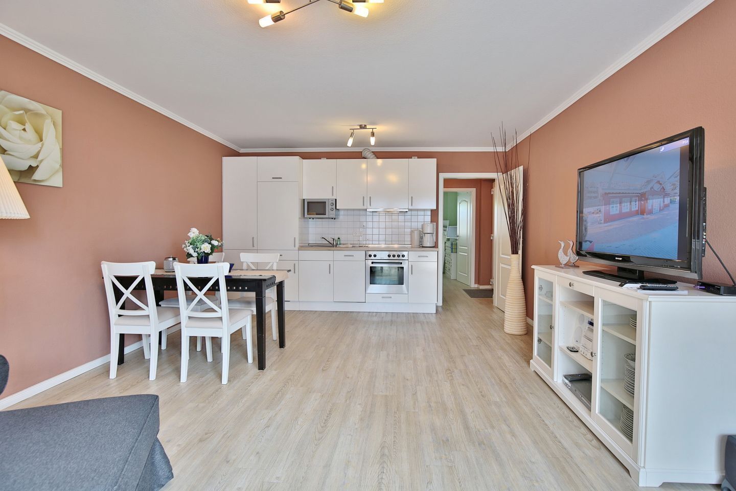 A modern kitchen with white cabinets, a dining area with a table and chairs, and a television on a cabinet.