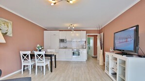 A modern kitchen with white cabinets, a dining area with a table and chairs, and a television on a cabinet. - Beach villa apartment 6 - Beach villa (Scharbeutz)