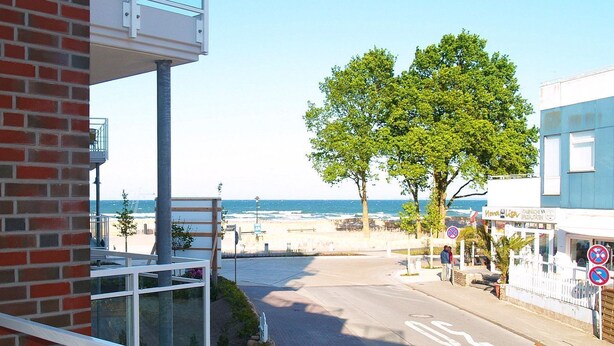 A coastal view from a balcony overlooking a beach, with a clear sky and a building with a blue facade in the background. - Beach villa apartment 14 - Beach villa (Scharbeutz)