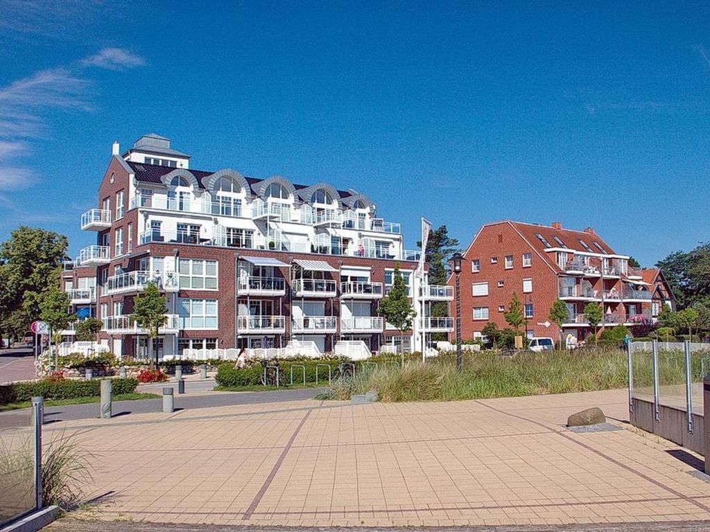Un immeuble d’appartements moderne doté de nombreux balcons, d’une allée pavée et surplombant un ciel d’un bleu éclatant.