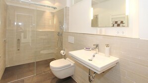 A modern bathroom with a glass-enclosed shower, a white sink with a mirror above, and a toilet.