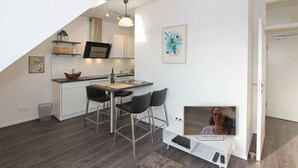 A modern kitchen with a dining area, a TV, and a small seating space.