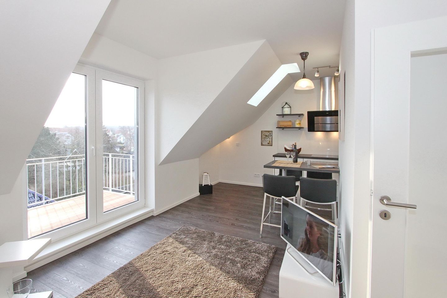 A modern loft apartment with a large skylight, a dining area with bar stools, and a kitchen with stainless steel appliances.