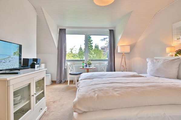 A bedroom with a bed, a TV, a desk, and a balcony with a view of trees.