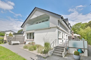 Ein zweistöckiges Haus mit Balkon, Veranda und einem kleinen Garten.
