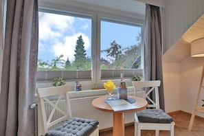 Ein Zimmer mit Tisch und zwei Stühlen, einem fenster mit Vorhängen und Blick auf Bäume und eine Pagode.