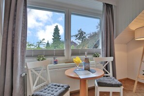A room with a table and two chairs, a window with curtains, and a view of trees and a pagoda.