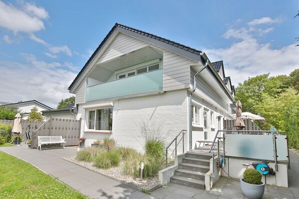 A two-story house with a balcony, a front porch, and a small garden area.