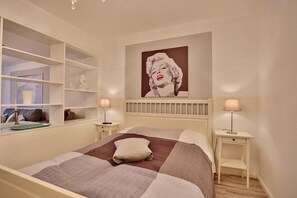 A bedroom with a large bed, two bedside tables, a nightstand, a wall-mounted shelf, and a large poster.