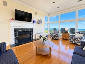 A spacious living room with a fireplace, a flat-screen TV, and a view of the ocean. - Goldenberg - 🏄Enjoy Spectacular Views from this 4 BR Oceanfront Home🏄 (Southern Shores)