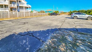 A parking lot with two cars, a wooden fence, and a building with balconies. - Goldenberg - 🏄Enjoy Spectacular Views from this 4 BR Oceanfront Home🏄 (Southern Shores)