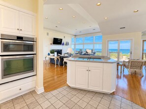 A kitchen with built-in ovens, a dining area with a view of the ocean, and a large window. - Goldenberg - 🏄Enjoy Spectacular Views from this 4 BR Oceanfront Home🏄 (Southern Shores)