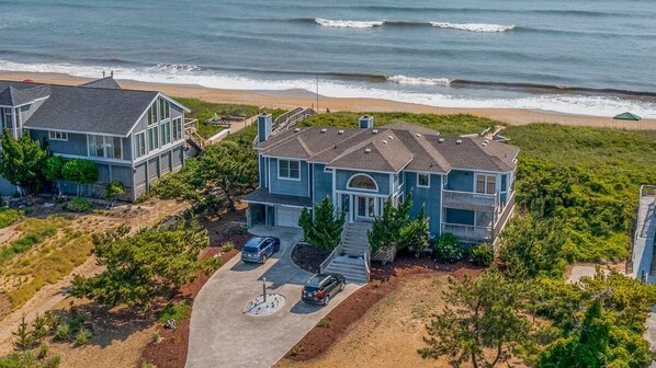 A coastal house with a large driveway, two cars parked, and a view of the ocean. - Goldenberg - 🏄Enjoy Spectacular Views from this 4 BR Oceanfront Home🏄 (Southern Shores)