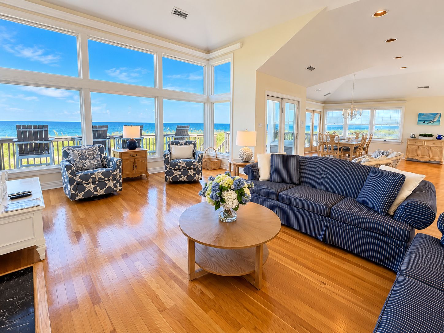 A spacious living room with a large window overlooking the ocean, a round wooden coffee table, and a striped sofa.
