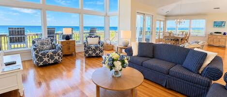 A spacious living room with a large window overlooking the ocean, a round wooden coffee table, and a striped sofa.