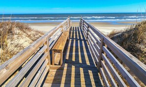 A wooden boardwalk leading to a beach with sand dunes and ocean views.