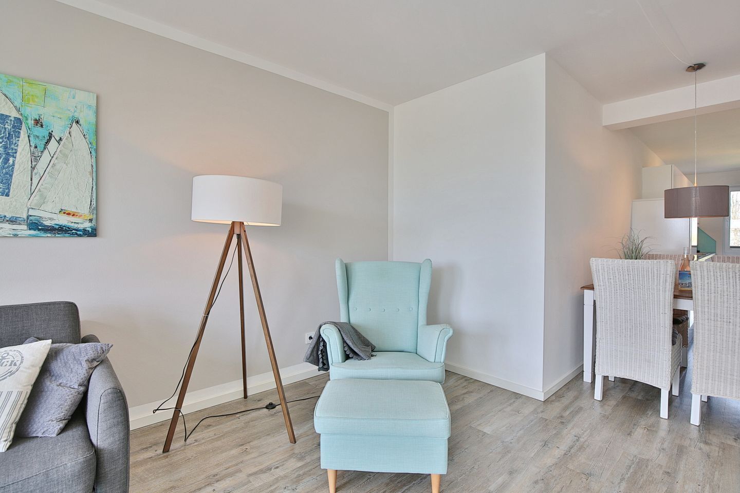 A modern living room with a light blue armchair, a floor lamp, and a painting of sailboats on the wall.