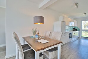 Una cocina moderna con armarios blancos, una mesa de comedor de madera, sillas de mimbre y una lámpara colgante.