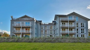 A multi-story residential building with balconies, a flat roof, and a grassy foreground.