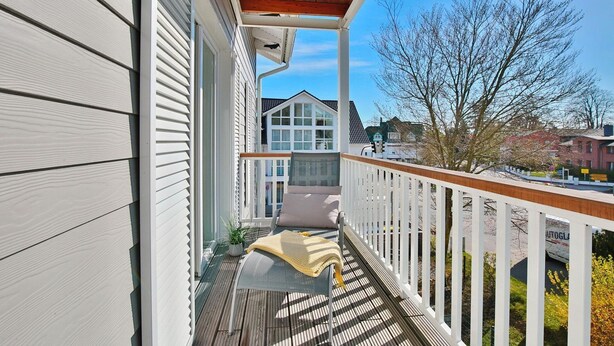 A wooden deck with a white railing, a bench, and a covered area with a wooden roof.
