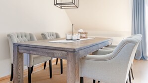 A dining area with a wooden table, grey upholstered chairs, a hanging light fixture, and a blue curtain. - Seestern Apartment 3 - Haus am Seehof 7 (Sierksdorf)