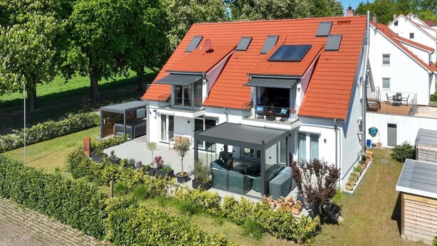 A modern two-story house with a red roof, large glass windows, and a spacious outdoor patio area. - Seestern Apartment 3 - Haus am Seehof 7 (Sierksdorf)