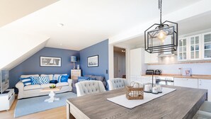 A modern living room with a wooden dining table, a sofa set, and a kitchen area with white cabinets and a wooden countertop. - Seestern Apartment 3 - Haus am Seehof 7 (Sierksdorf)