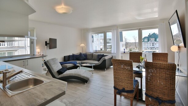 A modern living room with a sofa, chairs, a dining table, and a kitchen area with a sink.