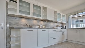 A modern kitchen with white cabinets, a wooden backsplash, and a window overlooking a balcony.