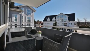 A balcony with wicker furniture and a potted plant, overlooking neighboring houses.