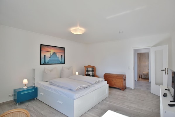 A modern bedroom with a bed, bedside tables, a wooden chest, and a painting on the wall.