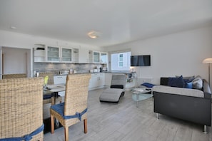 A modern living room with a grey sofa, a glass coffee table, and wicker chairs.