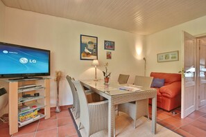 A living room with a television, wicker furniture, a red sofa, and a dining table. - Ferienhaus Seeweg - Ferienhaus Seeweg 4 (Scharbeutz)
