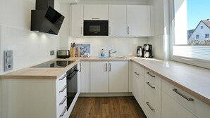Une cuisine moderne avec des meubles blancs, un four à micro-ondes, un évier et une fenêtre donnant sur des maisons.