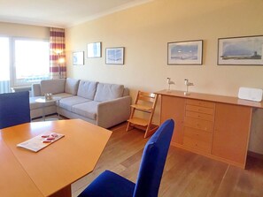 Una habitación de hotel moderna con sofá, una mesa de comedor, un escritorio de madera y una silla. Hay cuadros en la pared y una lámpara sobre la mesita de noche.
