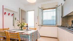 Un coin repas avec une table dressée pour deux personnes, des chaises en bois, un vase avec des fleurs et une fenêtre à barreaux.