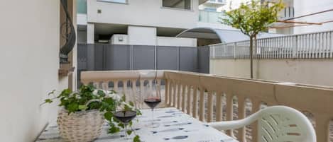 A balcony with a table set for two, a wicker basket, and a potted plant.