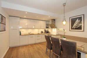 A modern kitchen with white cabinets, a wooden dining table, and two chairs. - Kurparkresidenz Apartment 14 - Kurparkresidenz (Scharbeutz)