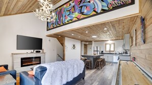 A modern living room with a fireplace, a large sofa, and a shuffleboard table. - Camelback Cabin 8  Poconos (Tannersville)