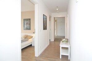 A hallway with a white sofa, a small table with a vase, and artwork on the walls. - Kurparkresidenz Apartment 13 - Kurparkresidenz (Scharbeutz)