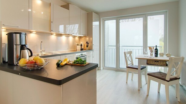 A modern kitchen with a central island, a dining area with a table and chairs, and a balcony with a view.