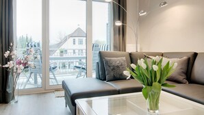 A modern living room with a sofa, a glass coffee table, and a view of a balcony with outdoor furniture.