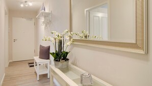 A hallway with a white bench, a potted orchid, a mirror with a decorative frame, and a door.