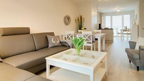 A modern living room with a sofa, a glass coffee table, and a dining area with white furniture.